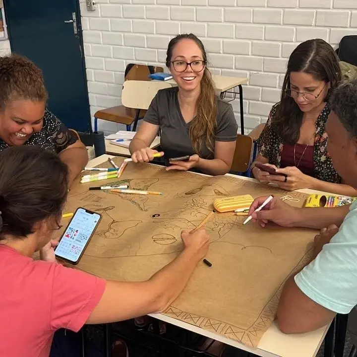 Estudantes desenham juntos sobre uma grande folha de papel pardo estendida nas mesas